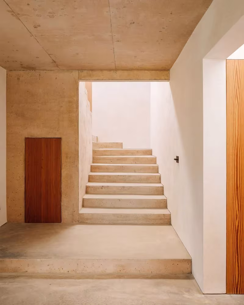 Escalera de hormigón claro entre muros blancos y techo de hormigón visto en la Casa 2 de Oporto