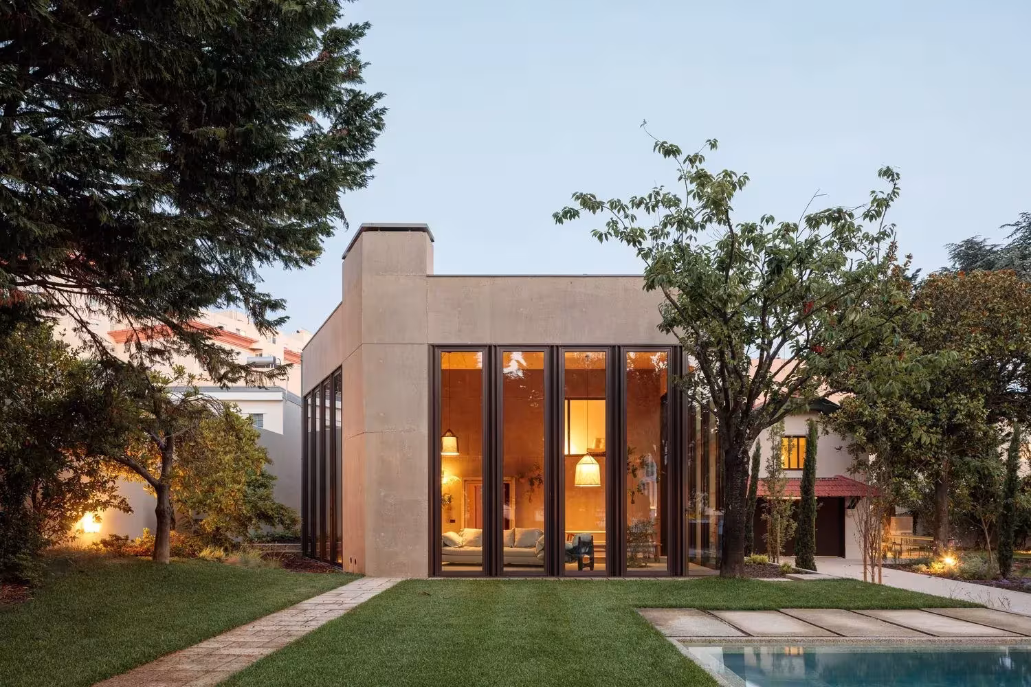 Casa 2 de Ricardo Bak Gordon al atardecer, con el interior iluminado tras las cristaleras y la piscina en primer plano
