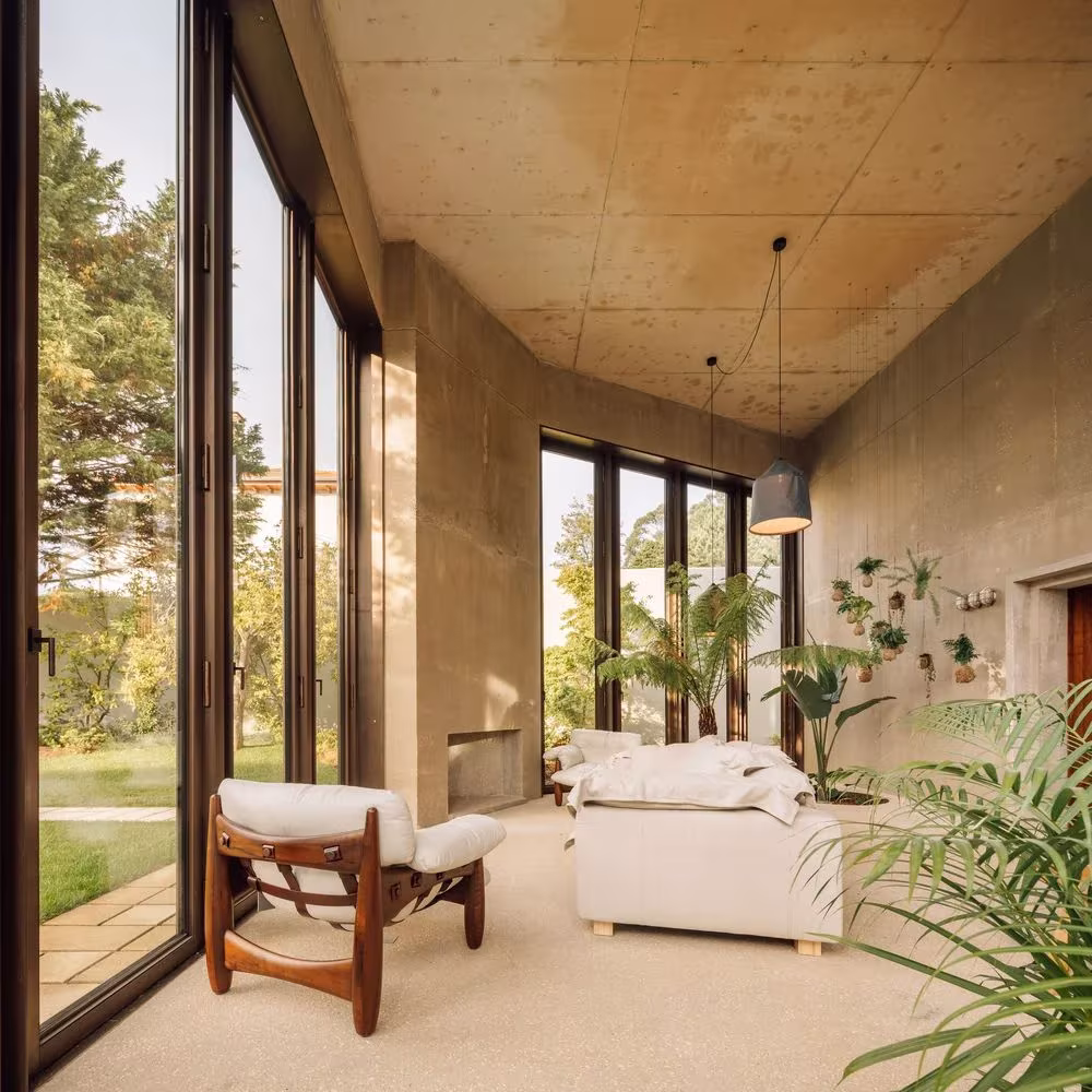 Jardín de invierno con paredes de hormigón y techo de madera, abierto con grandes ventanales en la Casa 2 de Oporto