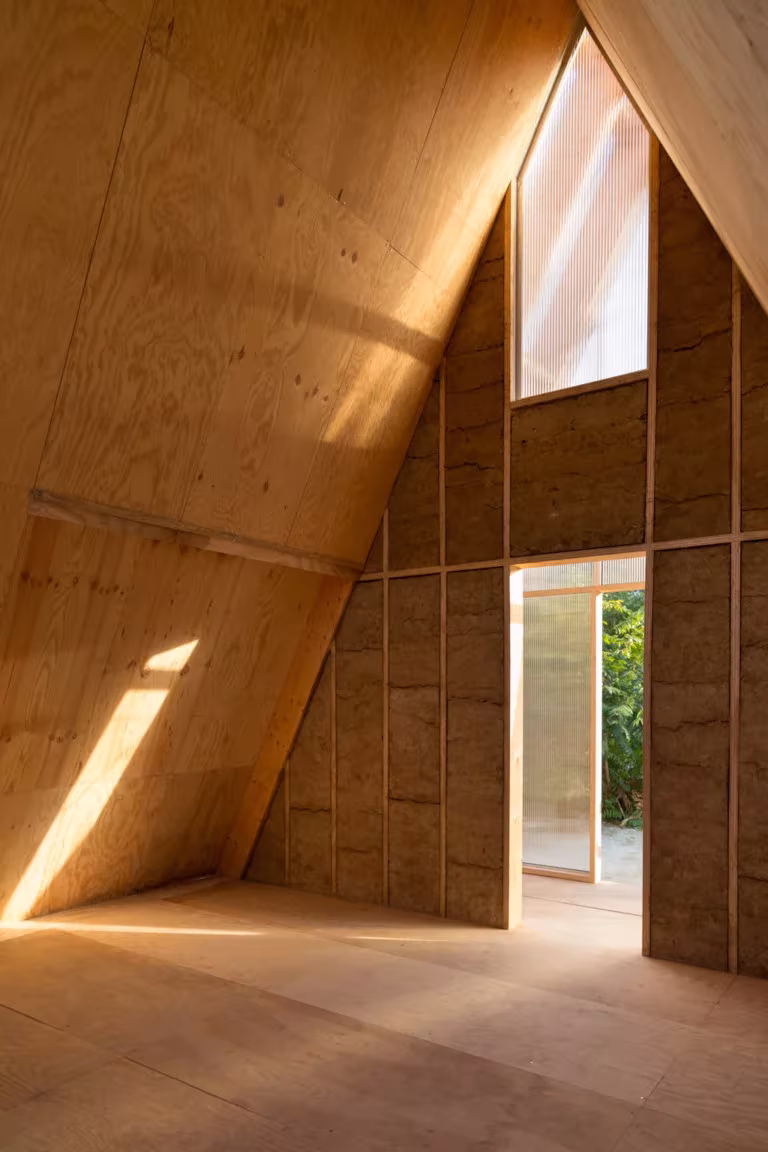 Interior triangular de madera del refugio Aire de Repos con ventana en el vértice y puerta acristalada
