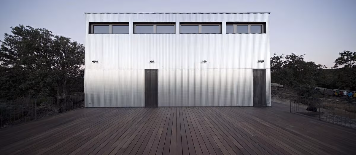Alzado de la Casa Garoza con ventanas altas en la parte superior y terraza de madera, en la sierra de Ávila