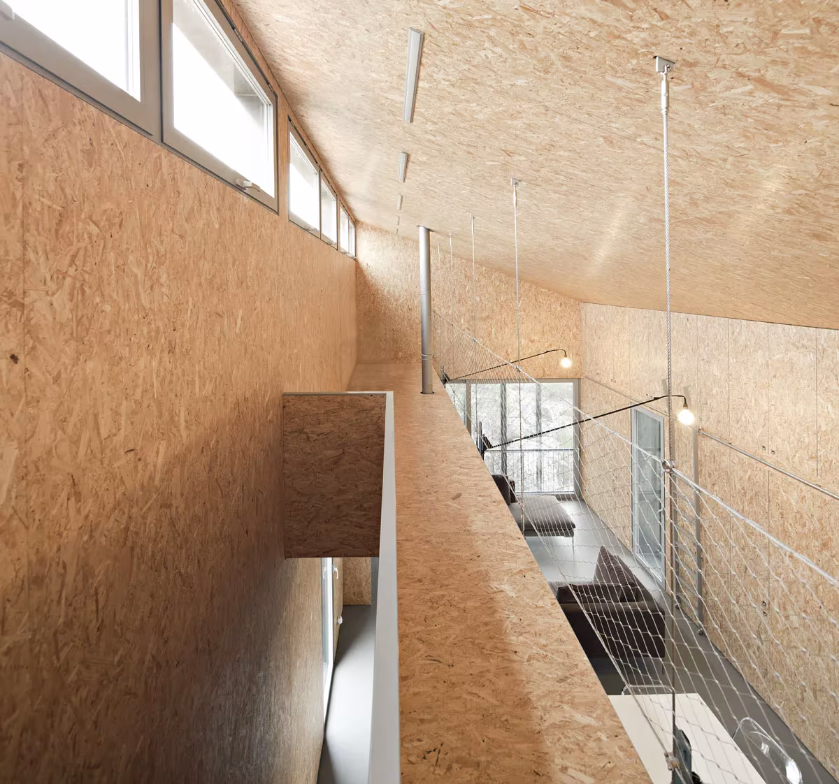 Interior de tablero OSB con ventanas altas y pasarela superior en la Casa Garoza, del Estudio Herreros