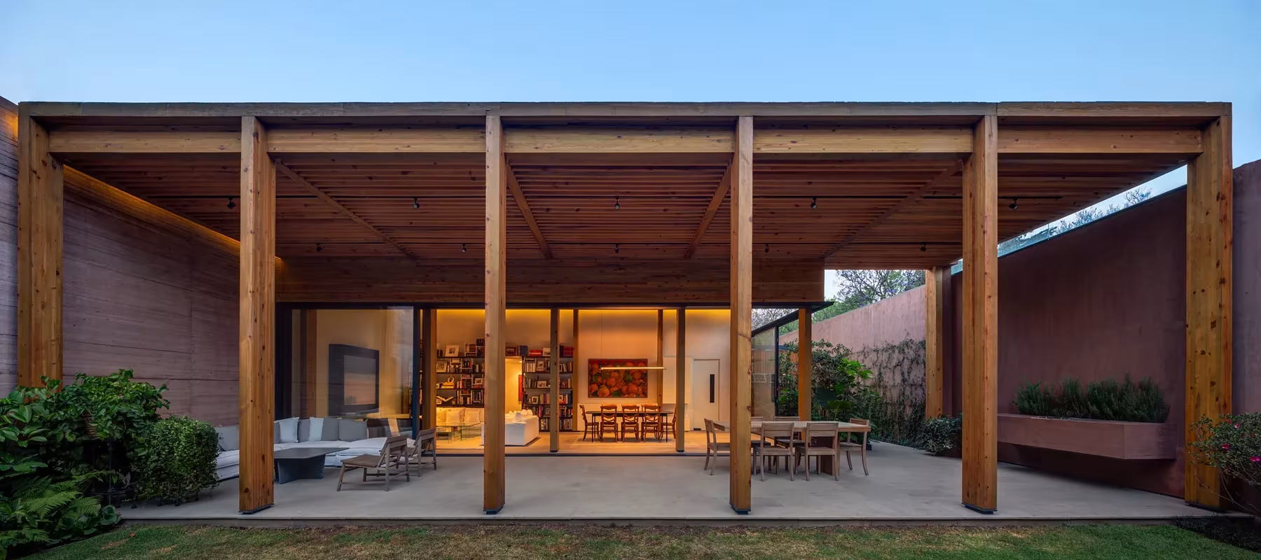 Porche de Monte Tauro de PPAA con pórtico de vigas de madera y salón iluminado al fondo