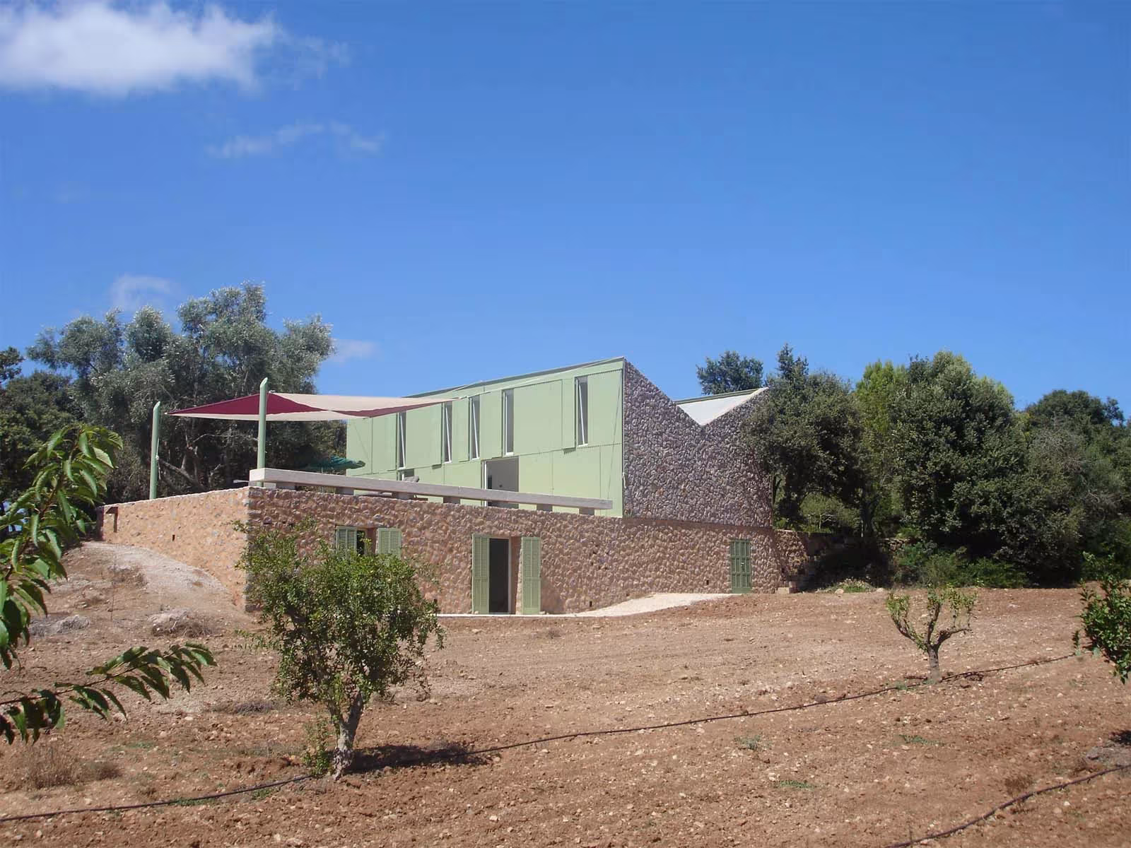 Casa Cobo del Estudio Herreros en Artá, volumen verde sobre muro de piedra seca entre olivos