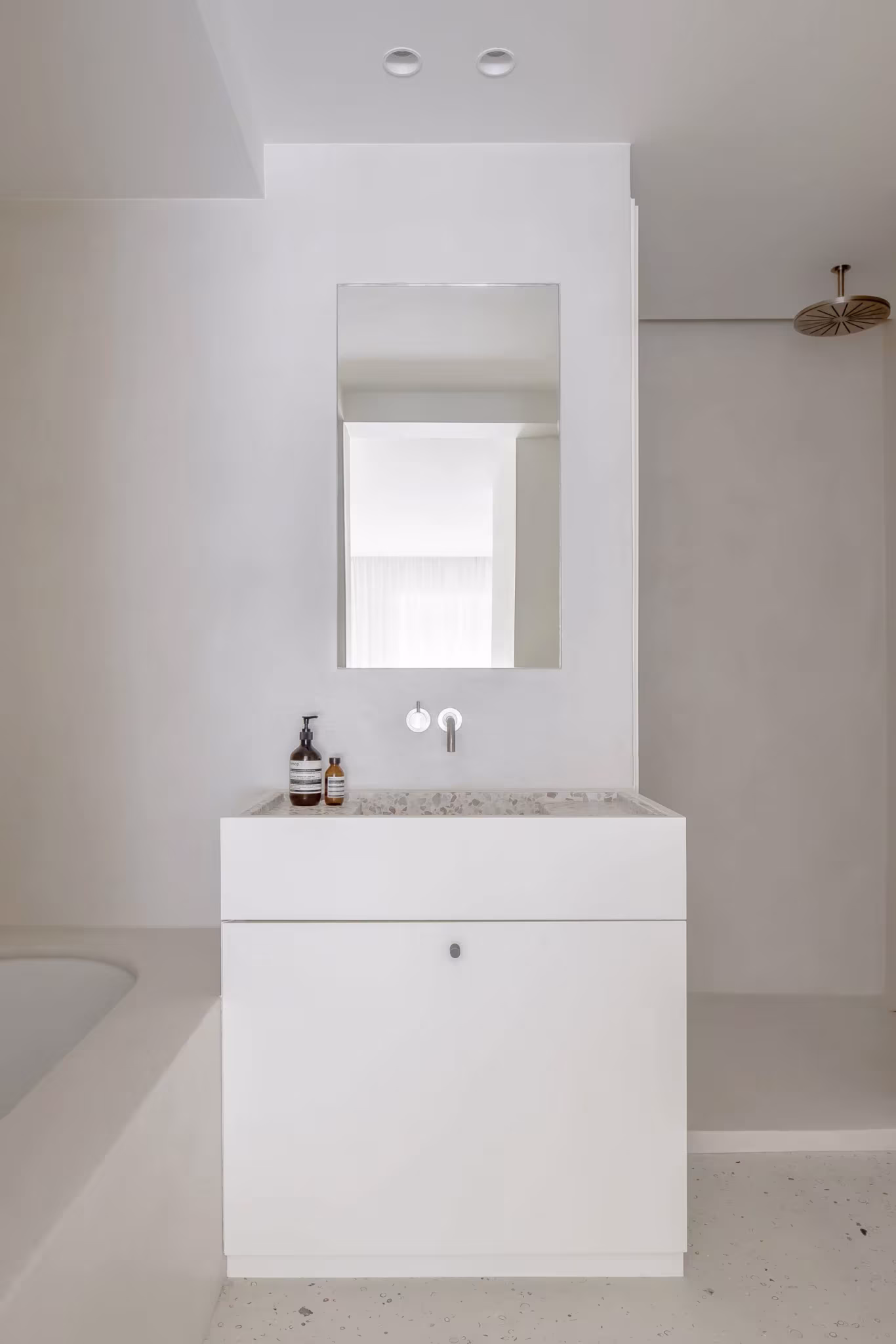 Baño blanco con lavabo sobre mueble, espejo vertical y grifería mural en el proyecto BUN de Nils Van der Celen