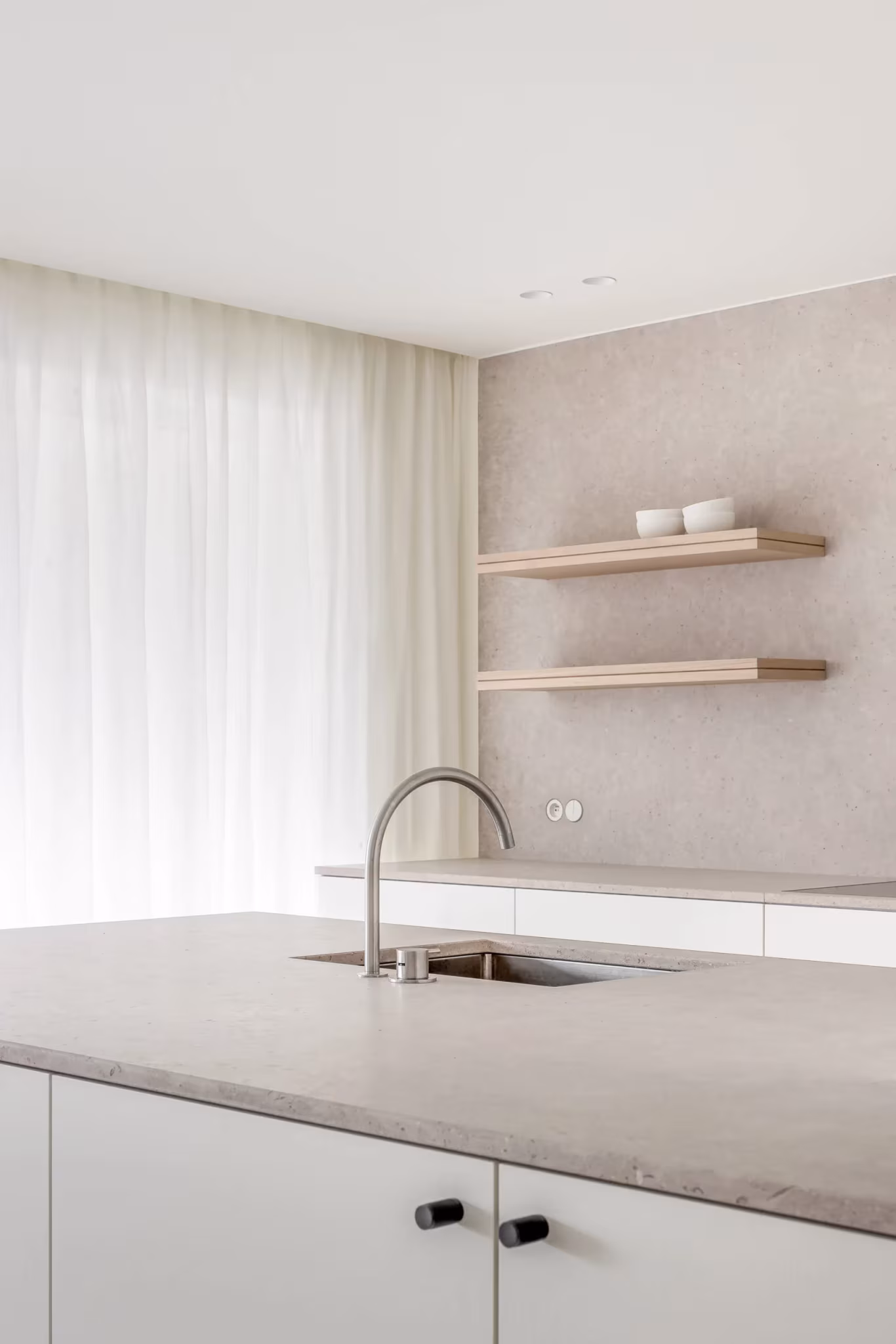 Isla de cocina con encimera de piedra y estantes de roble junto a cortinas de lino en el proyecto BUN, Knokke