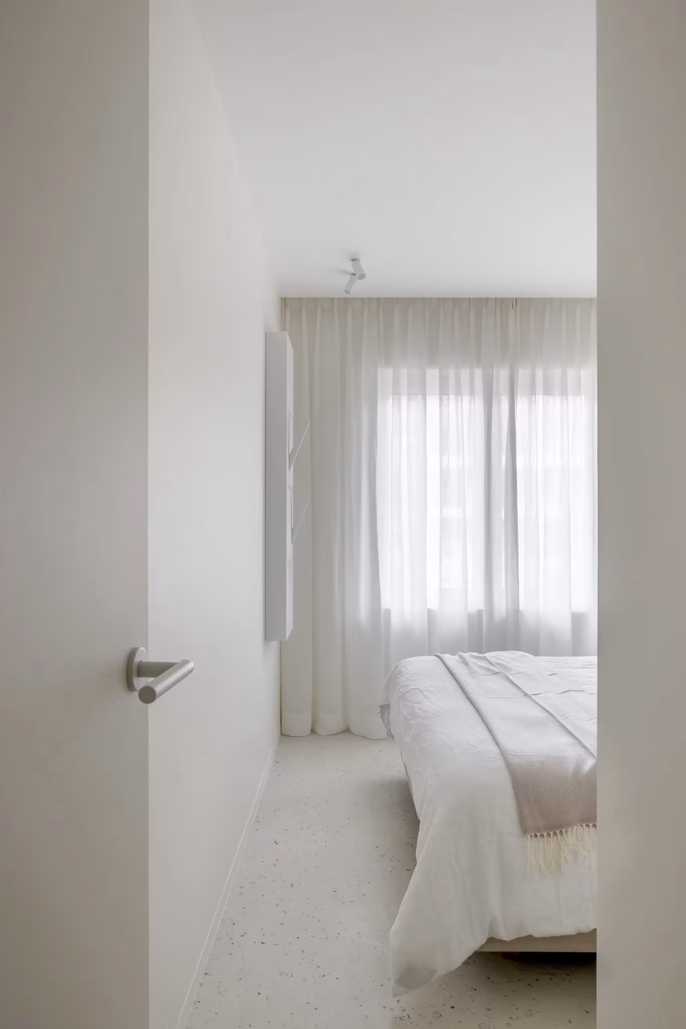 Dormitorio blanco con cortinas ligeras visto desde la puerta en el proyecto BUN de Nils Van der Celen
