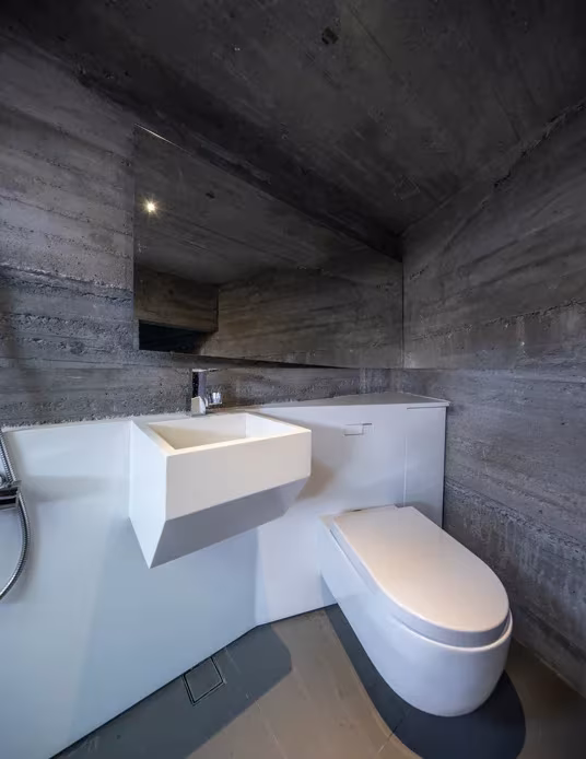 Baño de hormigón visto con lavabo y sanitarios blancos en una vivienda de Micro Hutong, de 35 m2