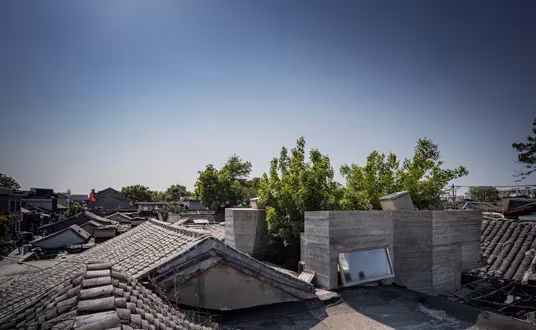 Cubierta de tejas del hutong con los volúmenes de hormigón de Micro Hutong asomando sobre los tejados de Pekín