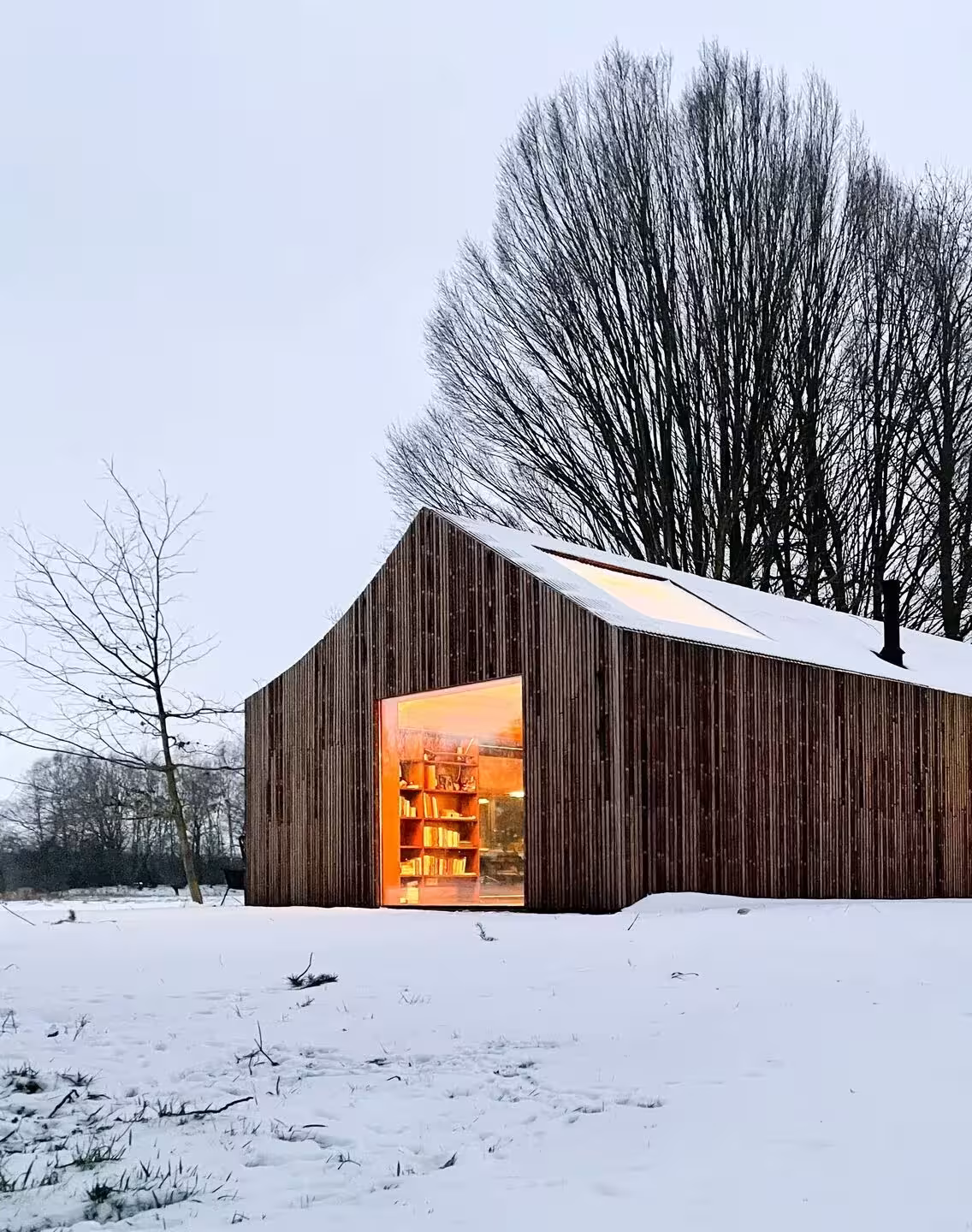 Shady Shed bajo la nieve con la biblioteca iluminada tras la gran apertura de la fachada