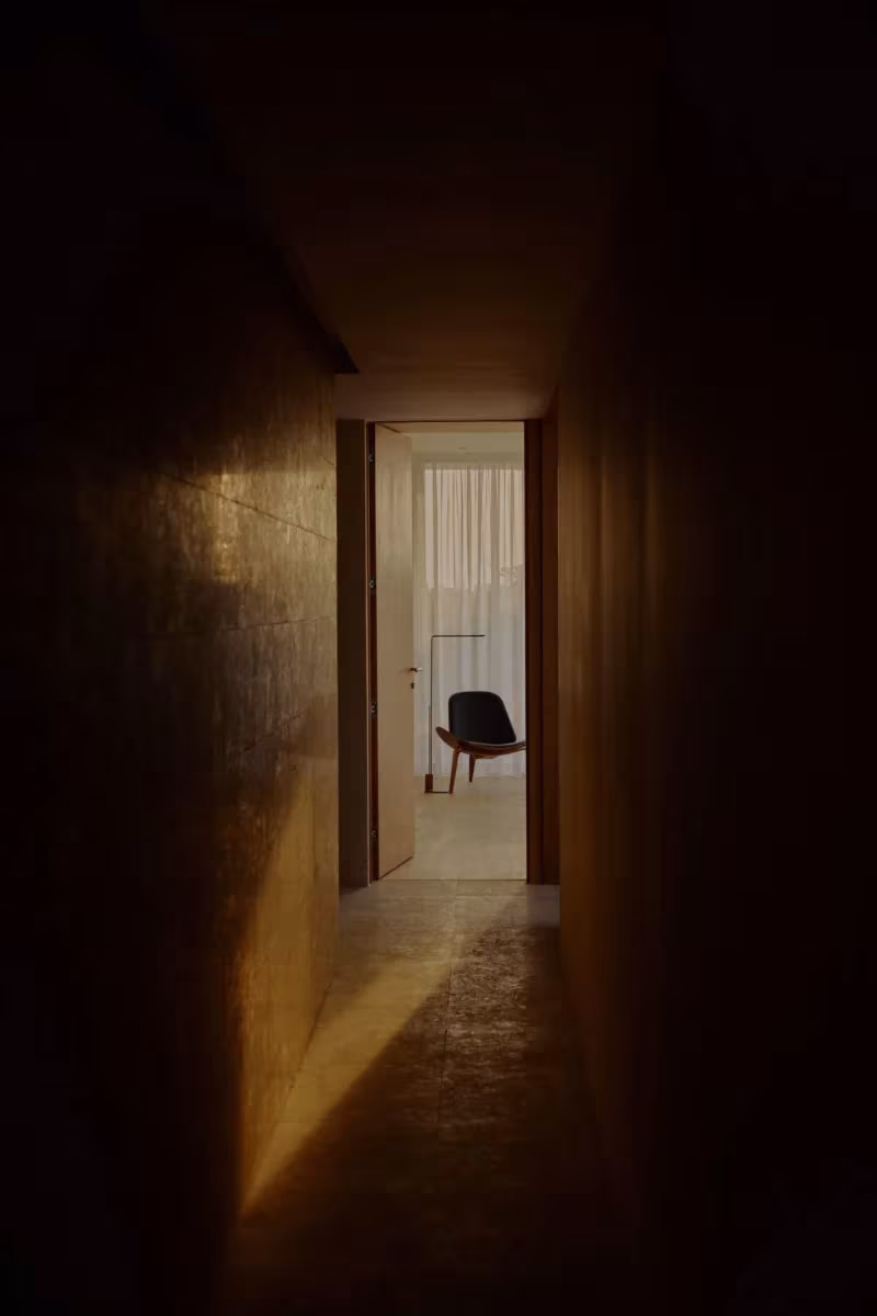 Corredor en penumbra de Villa AM, con luz dorada al fondo sobre una silla, obra de MESURA en Jeddah