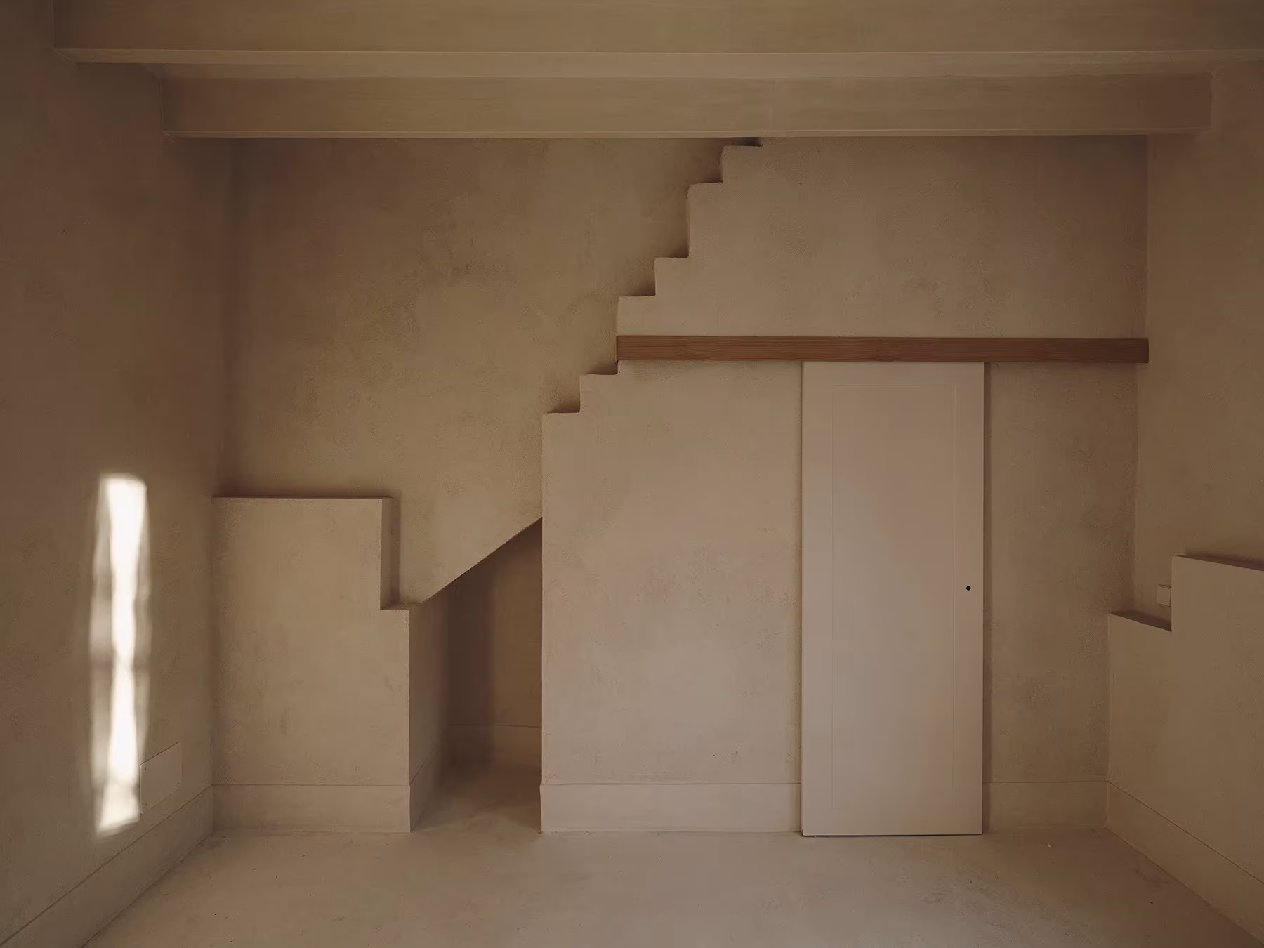 Escalera de obra bajo la que se integra un armario, en un interior encalado de la rehabilitación de Can Monges, Mallorca