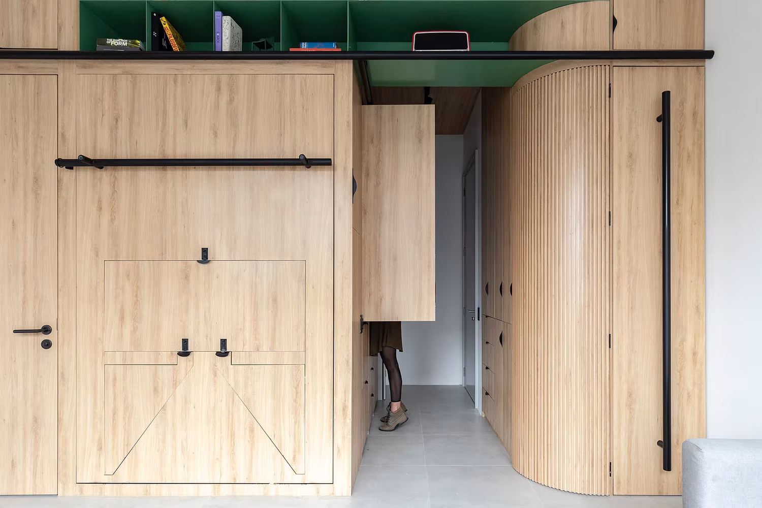 Mueble de madera con puerta y esquina curva que oculta una cama y una zona de almacenaje, en Doméstico