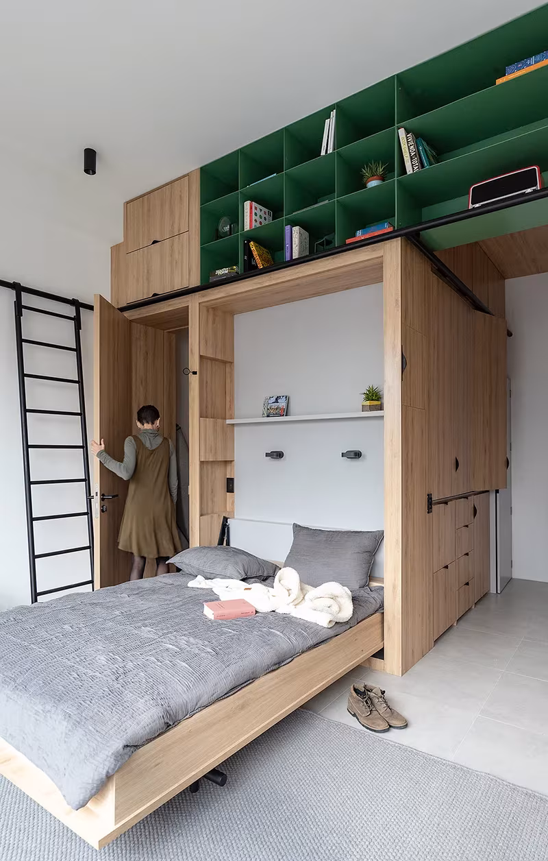Cama abatible desplegada bajo las estanterías verdes del módulo de madera de Doméstico