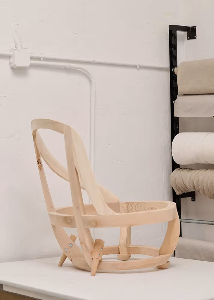 Estructura de madera de la butaca Elena de Helena Rohner para Rabadán, junto a rollos de tela en el taller