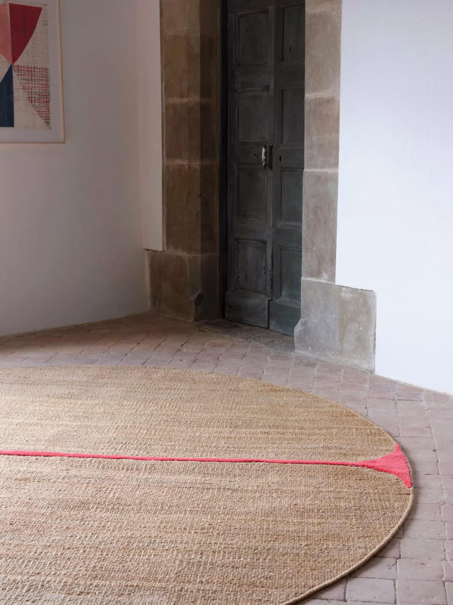 Alfombra redonda de fibra natural con un reborde rosa junto a un muro de piedra, en el espacio de Rabadán