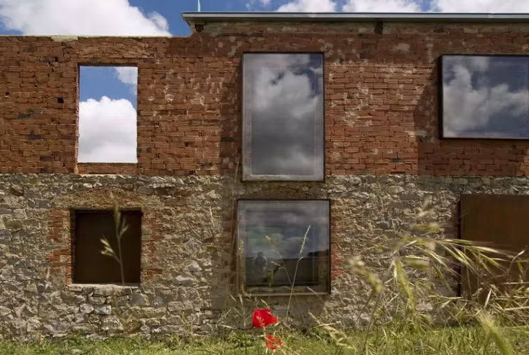 Fachada de piedra y ladrillo con ventanas de gran formato que reflejan el cielo en La ruina habitada