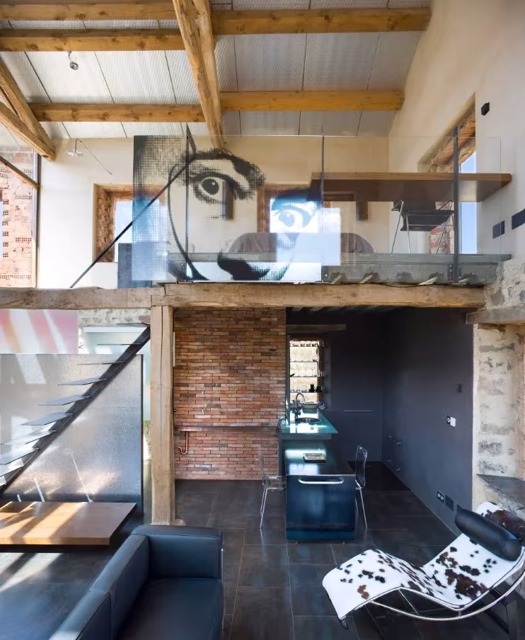 Salón de doble altura con vigas de madera, muro de ladrillo y pasarela de vidrio en La ruina habitada