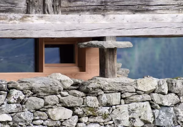 Ventana de la cabaña de Sarrayer entre un muro de piedra seca y una viga de madera
