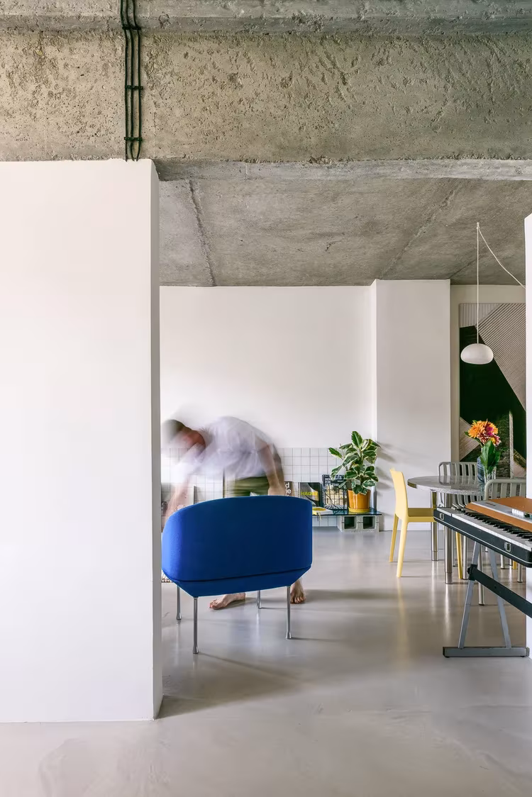 Loft de Casa I O en Bratislava con techo de hormigón visto, butaca azul y persona en movimiento