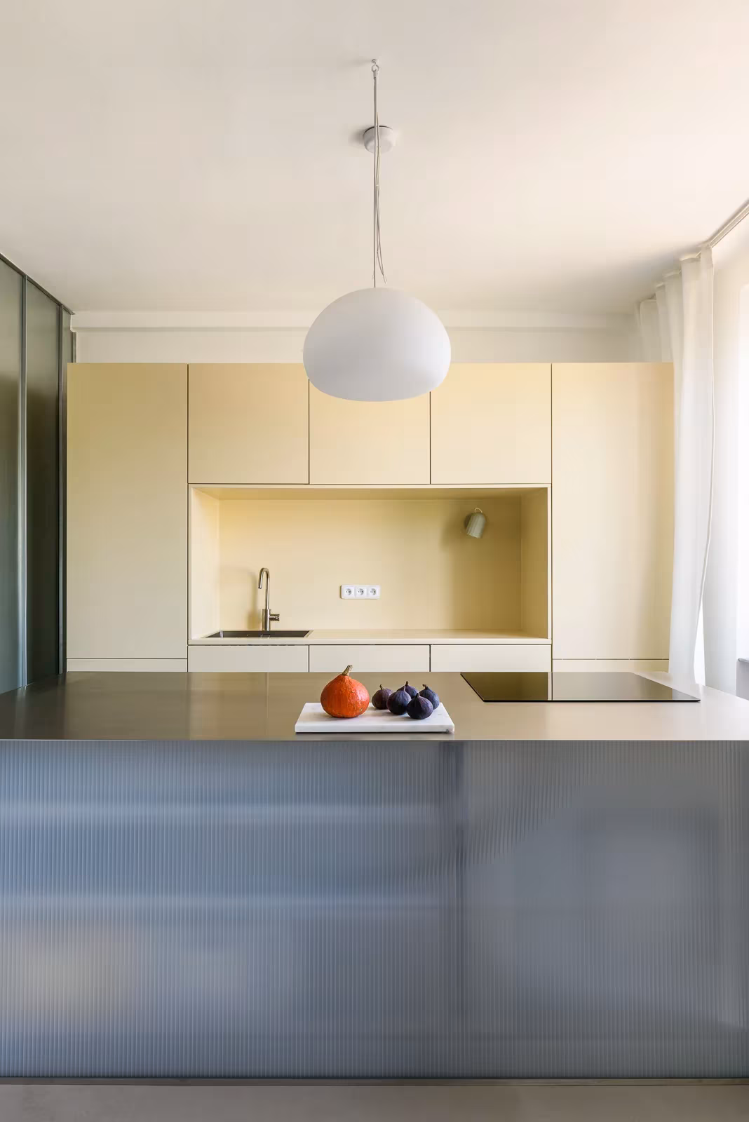 Cocina de Casa I O de Alan Prekop con isla de acero, muebles amarillo claro y lámpara blanca