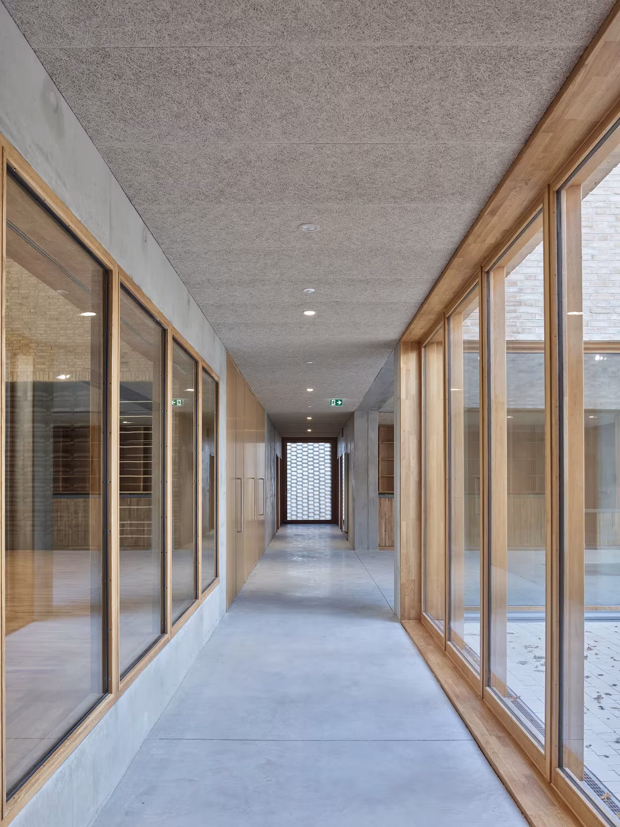 Pasillo de hormigón con ventanas de madera a ambos lados en el polideportivo de RAUM en Saint-Jean-de-Boiseau