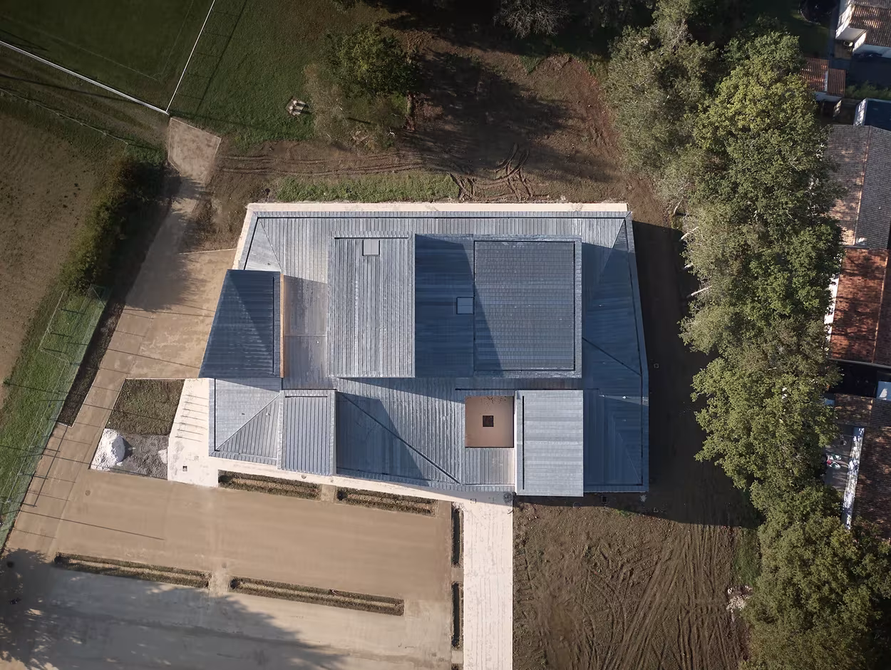 Vista aérea de las cubiertas metálicas del polideportivo de RAUM junto a una masa de árboles