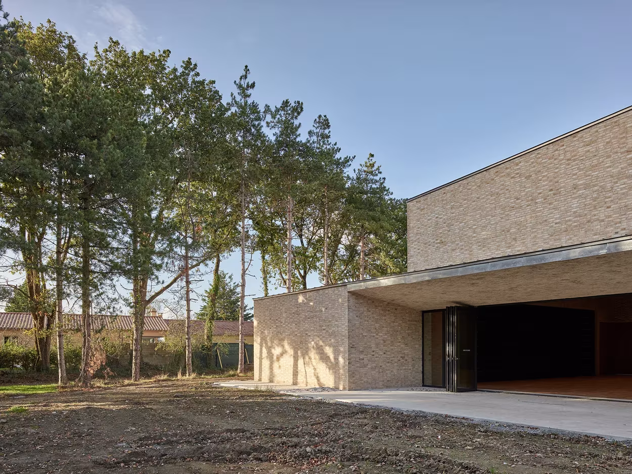 Entrada cubierta de ladrillo claro entre pinos en el polideportivo de RAUM, cerca de Nantes