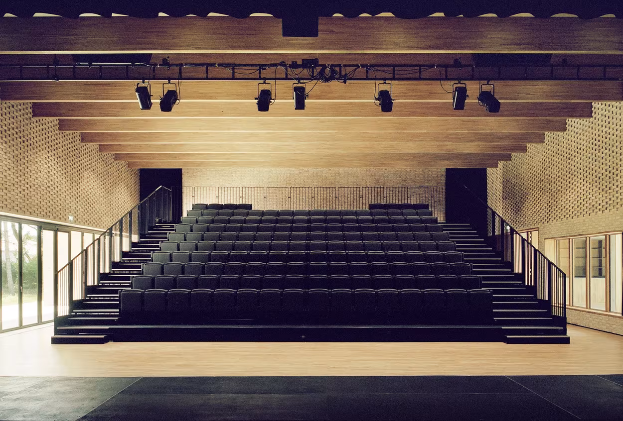 Sala con gradas y techo de vigas de madera iluminada para espectáculos en el polideportivo de RAUM