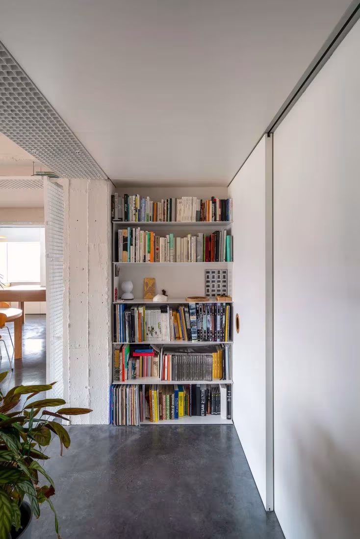 Estantería de libros al fondo de un pasillo con suelo de hormigón en la reforma de Pachón-Paredes, Madrid
