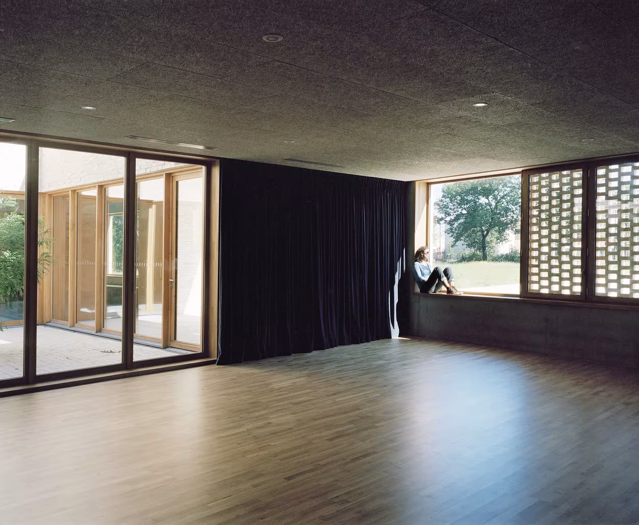Sala de suelo de madera con cortina negra y ventanales de carpintería en el polideportivo de RAUM