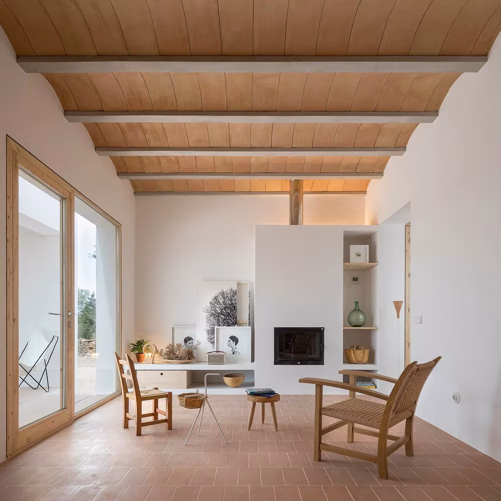 Salón con chimenea sobre muro exento, butacas de enea y techo de vigas y cerámica en Es Pou