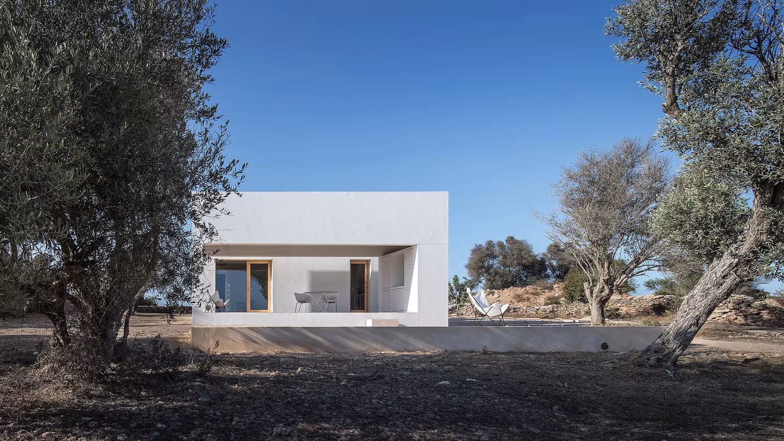 Fachada blanca de Es Pou entre olivos, con porche y tumbonas, en Formentera