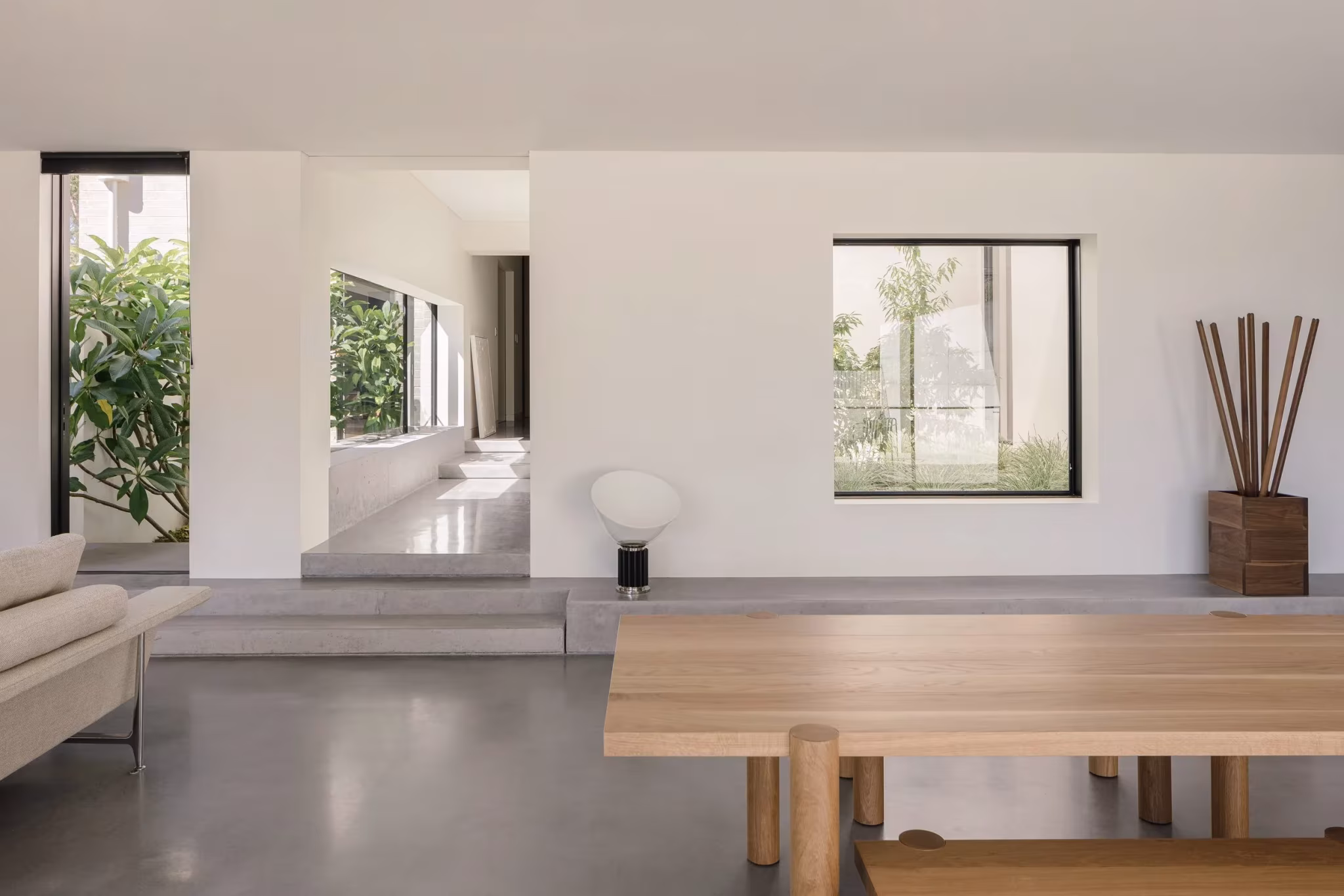 Salón de líneas depuradas con mesa de madera, sofá y ventanas al jardín en la casa de Whispering Smith