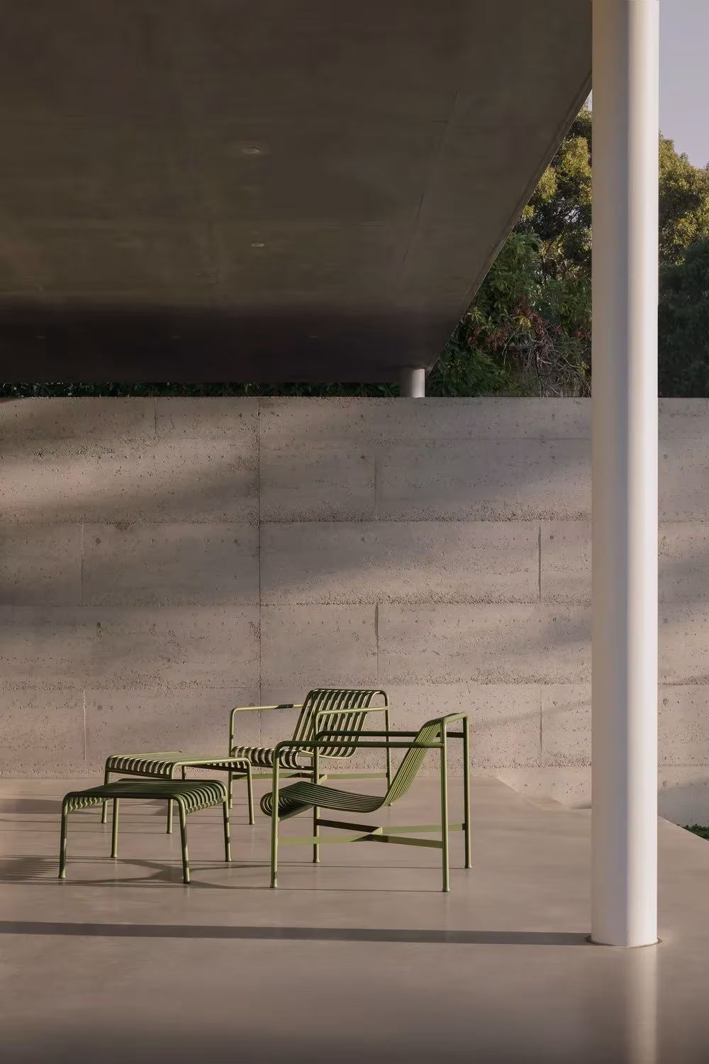 Porche de hormigón con pilar blanco y sillas verdes de exterior en la casa de Whispering Smith