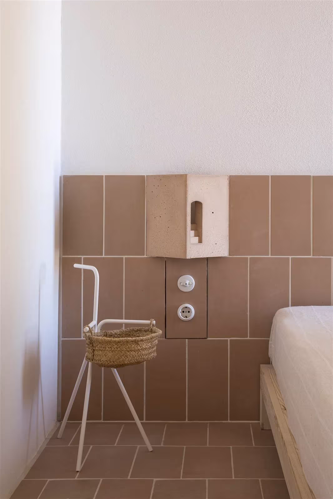 Cabecero de baldosas terracota con aplique y una silla con cesto junto a la cama en Es Pou
