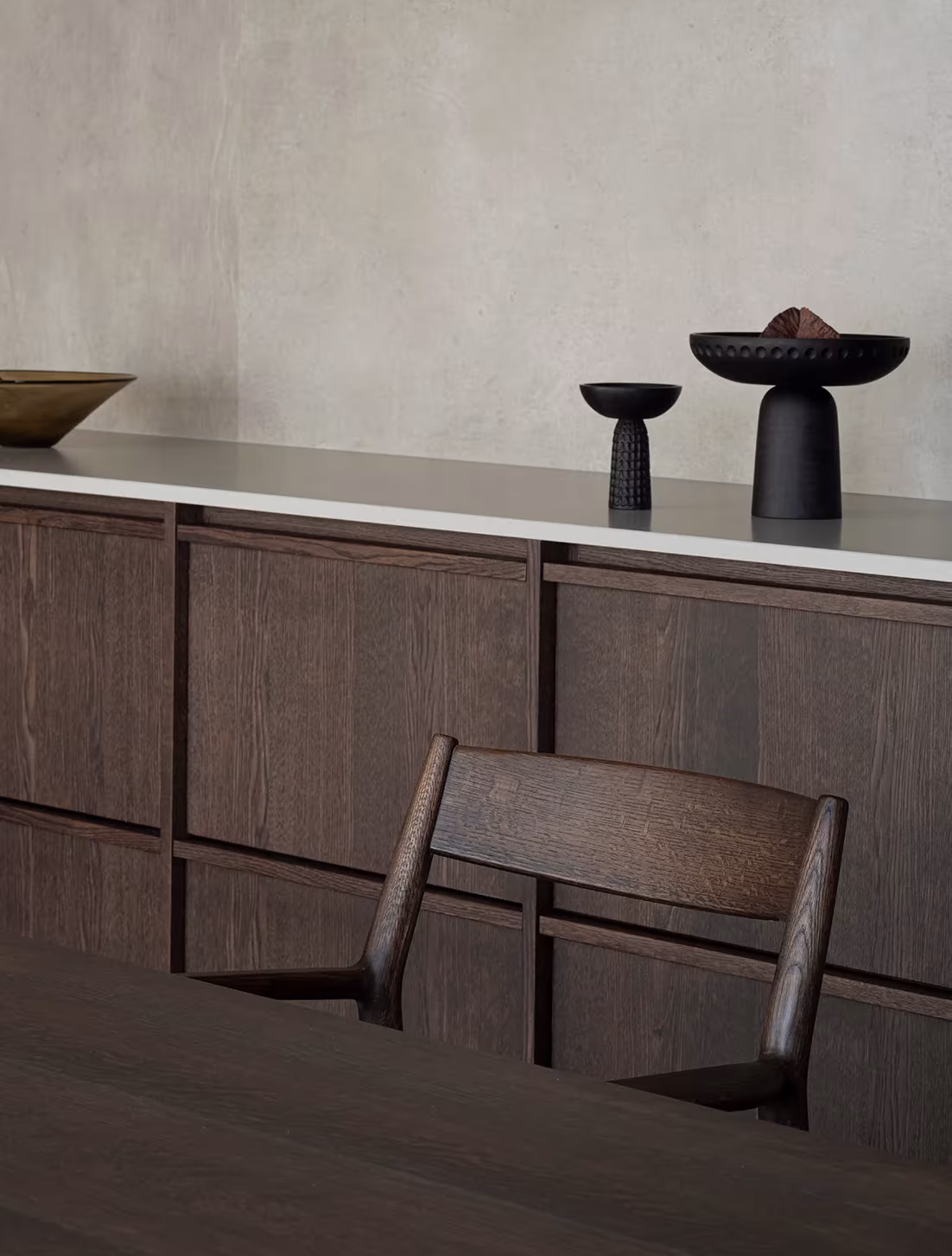 Aparador de roble tintado oscuro con cuencos de cerámica negra y silla de madera en la Azabu Residence de Norm Architects