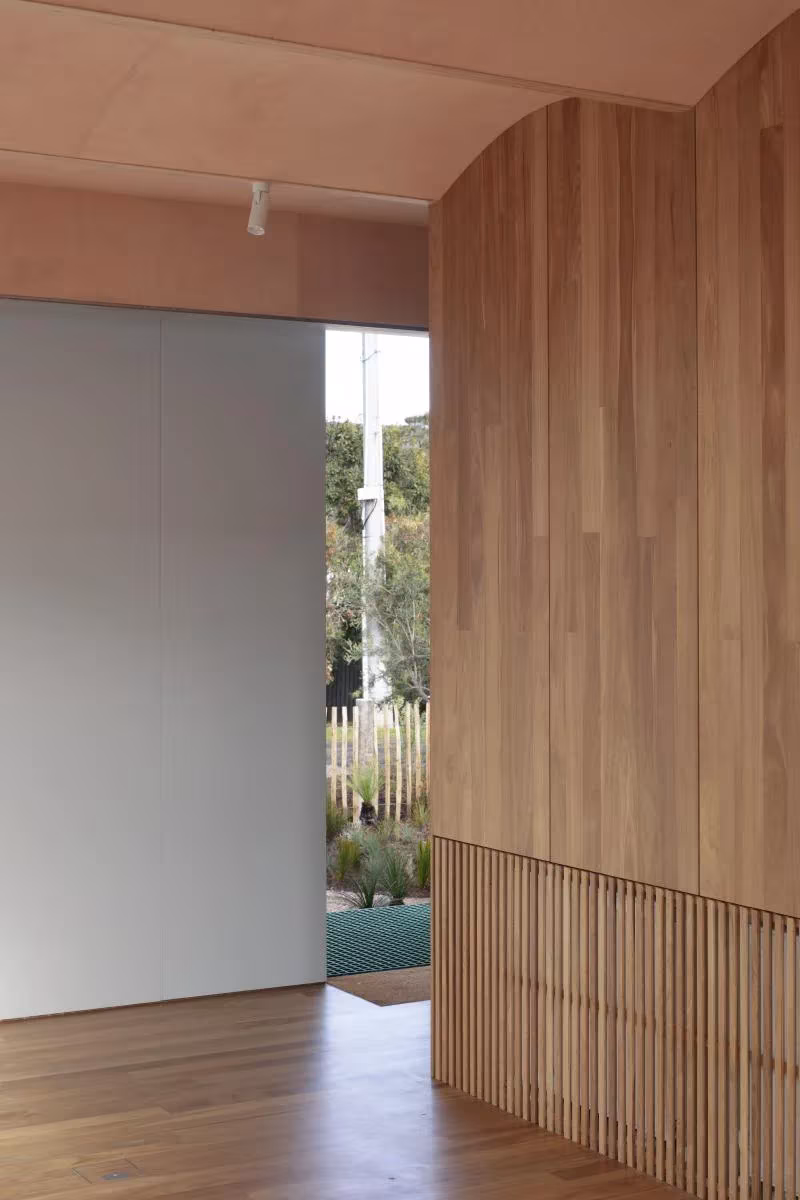 Muro curvo de lamas de roble y suelo de madera que dan paso al exterior en la Casa AB de Barwon Heads