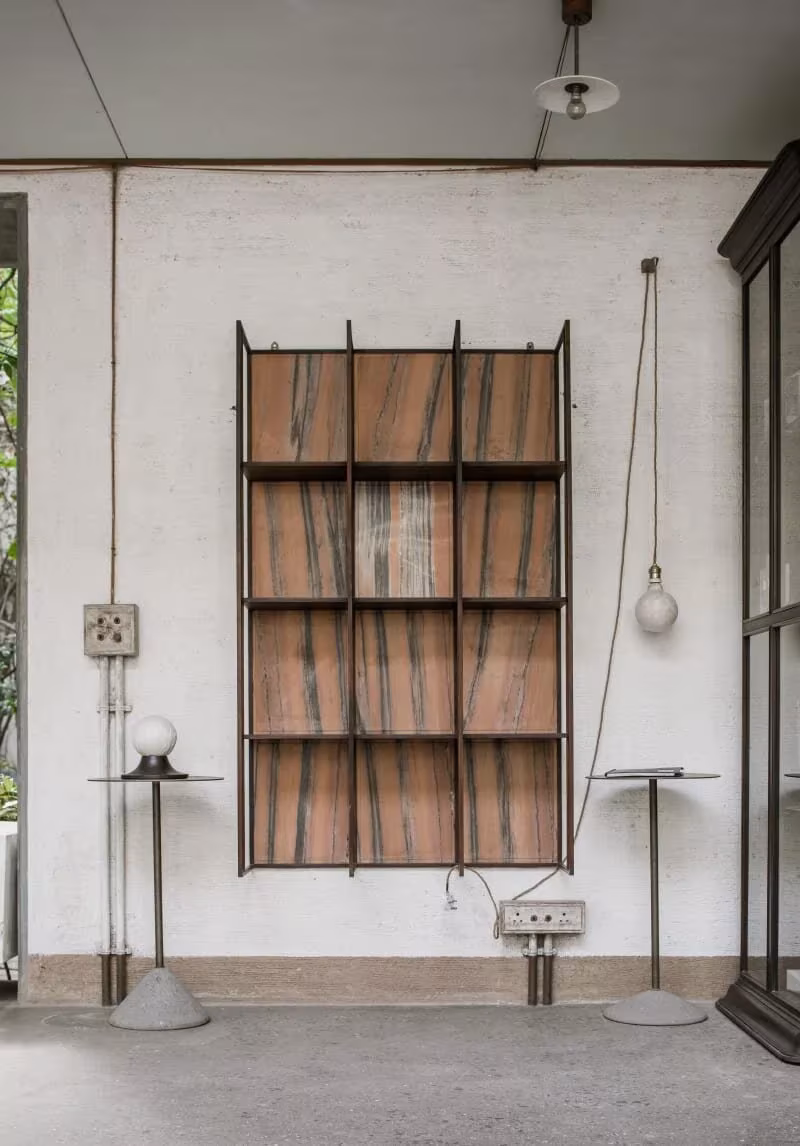 Estantería de madera y hierro sobre un muro encalado con cableado visto en el atelier de Studio Mumbai, Alibag