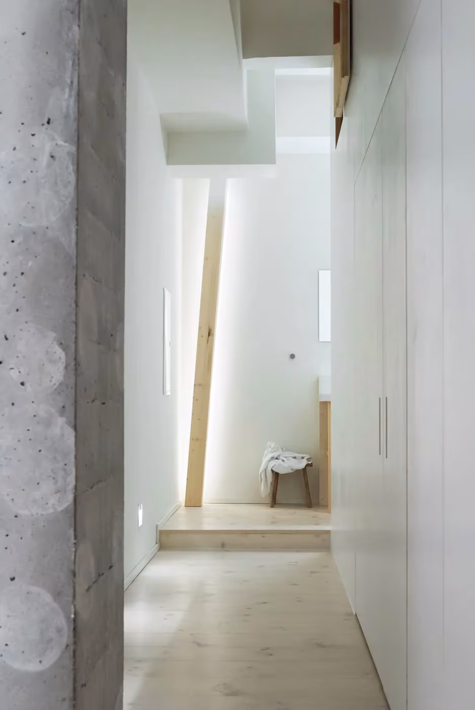 Pasillo de hormigón y paño blanco que conduce a un escalón de madera clara en The Garden Room del hotel Michelberger