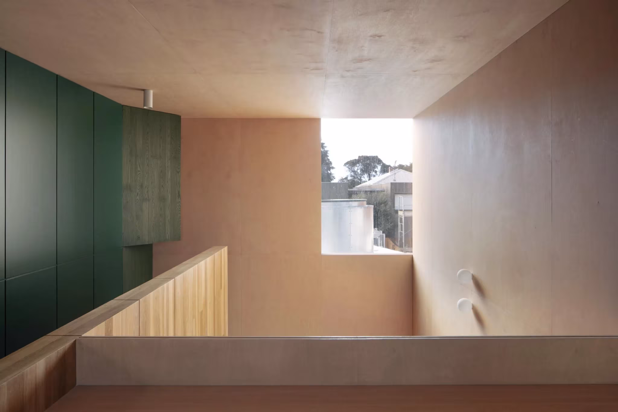 Estancia revestida de contrachapado con armario verde y ventana apaisada sobre la barandilla en la Casa AB, Australia