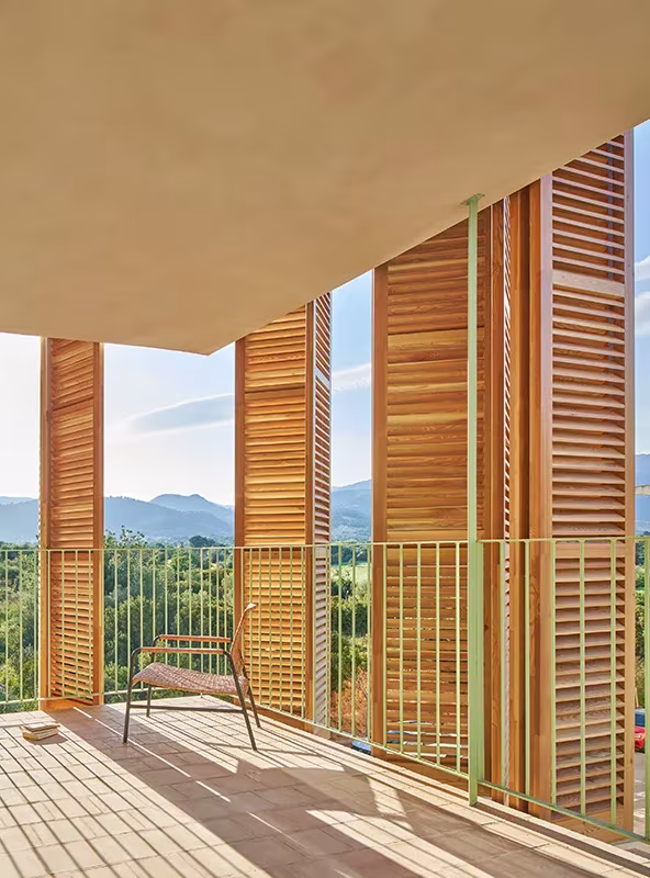 Balcón con contraventanas de madera abiertas, silla y vistas a la sierra en las viviendas de Inca