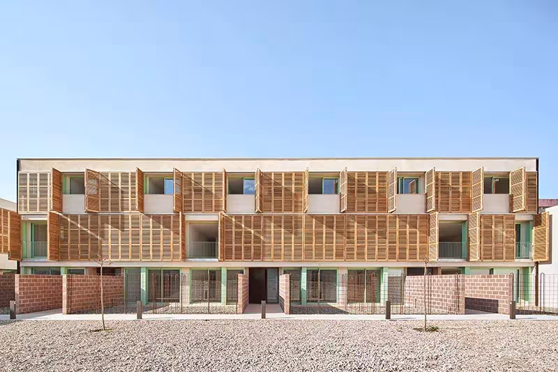 Fachada larga de las viviendas de Alventosa Morell con contraventanas de madera abiertas y planta baja de ladrillo