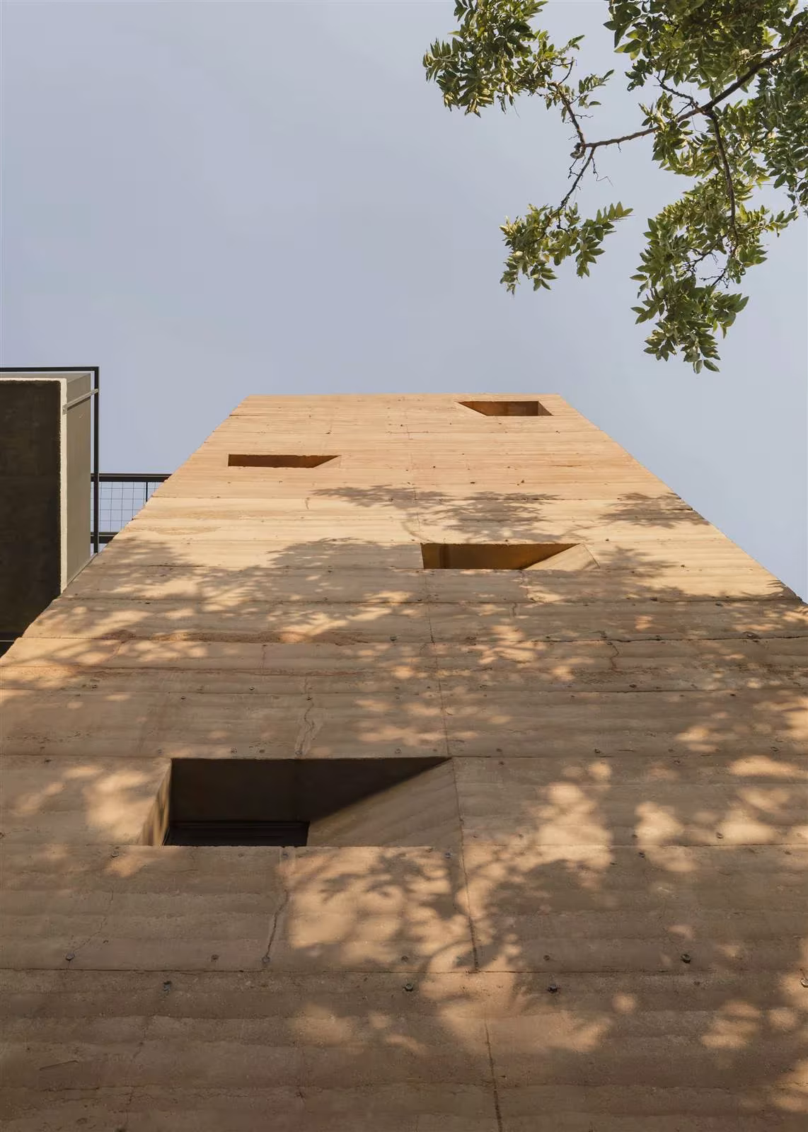 Muro de tierra compactada del Edificio Valois de José Cubilla con ventanas abocinadas y sombras de hojas