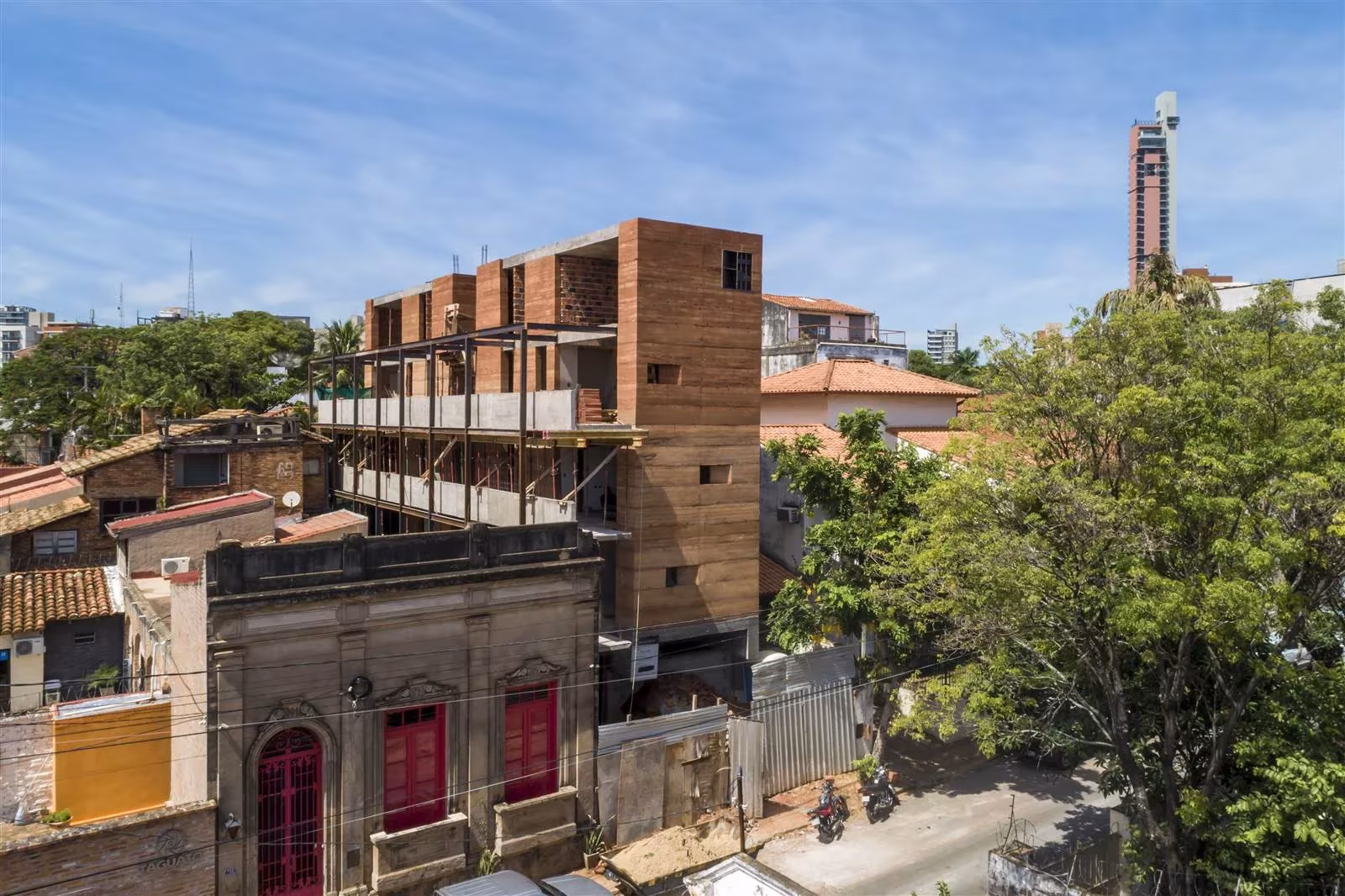 Edificio Valois en construcción con muros de tierra compactada sobre casas bajas y árboles del barrio
