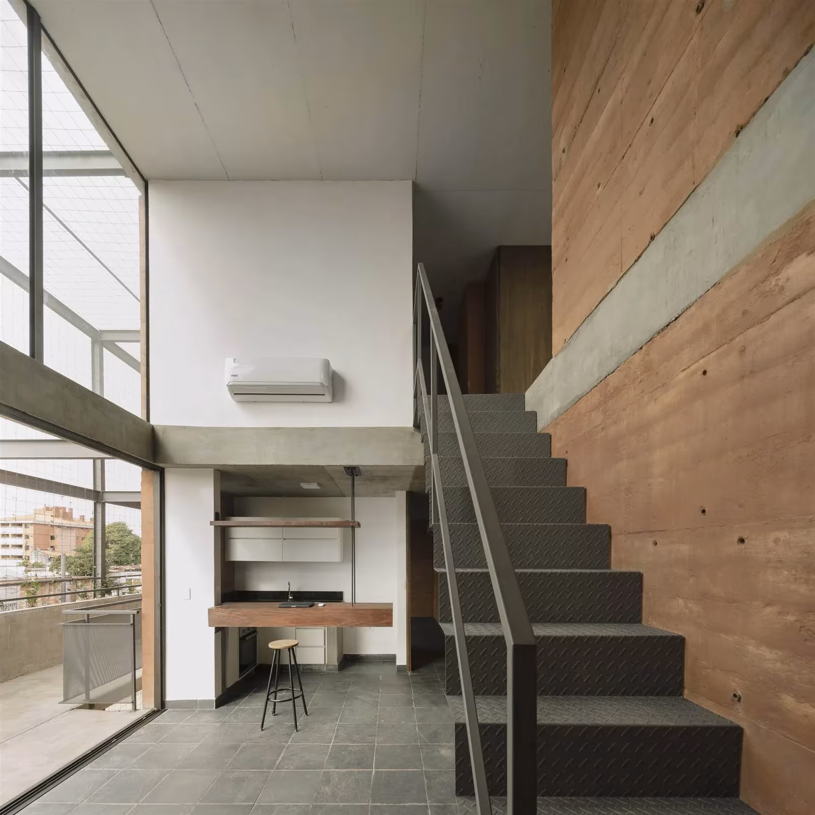 Dúplex del Edificio Valois con escalera metálica junto a muro de tierra compactada y gran ventanal