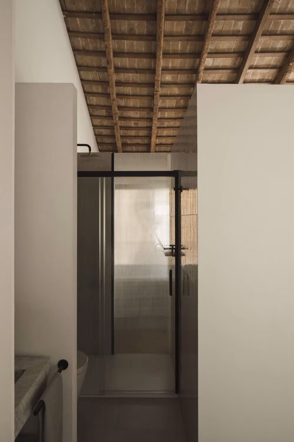 Hueco de escalera con puerta de vidrio bajo un techo de viguería antigua en la Casa del Calvari de Endalt