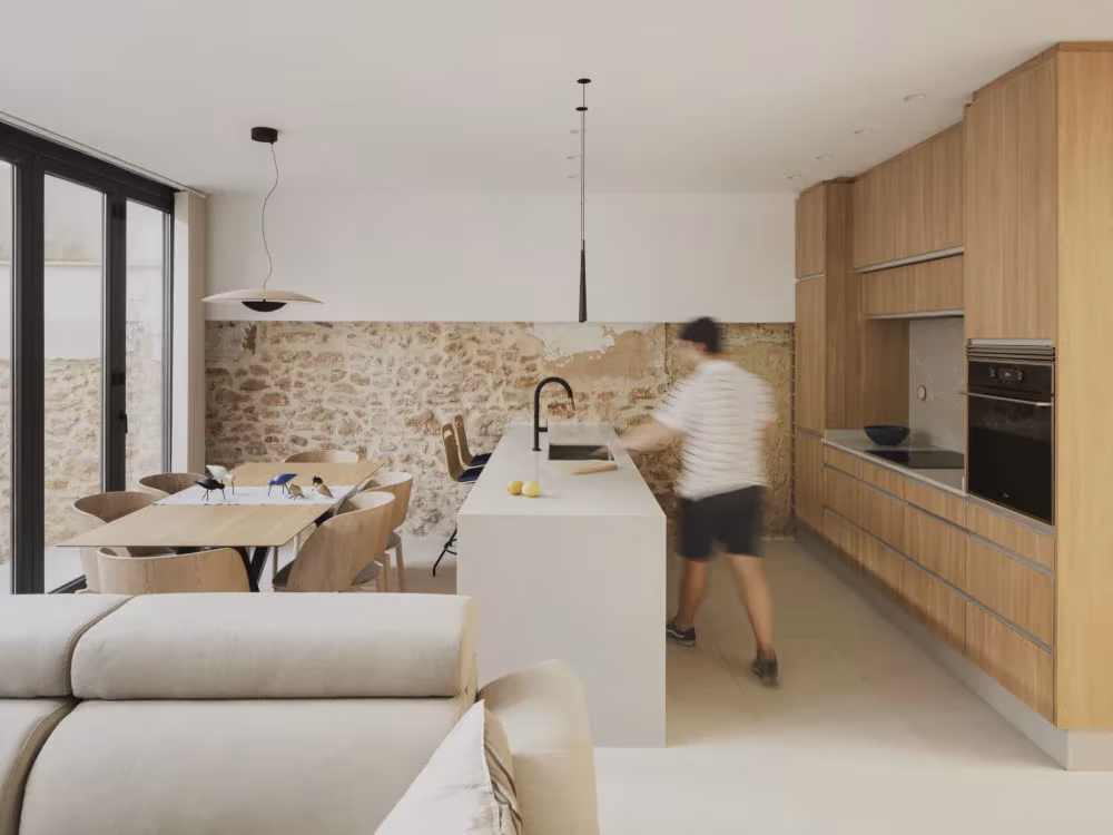 Cocina de roble con isla blanca y comedor junto al muro de piedra original en la Casa del Calvari, Alcàsser