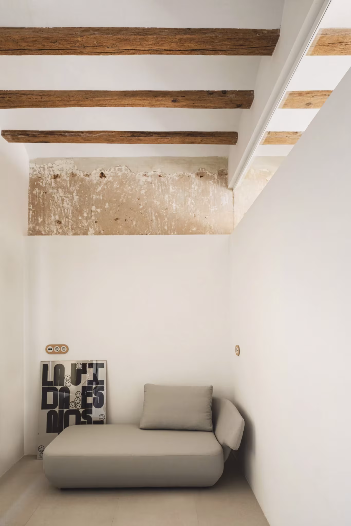 Rincón de lectura con chaise longue bajo vigas de madera y muro de piedra visto en la Casa del Calvari de Endalt