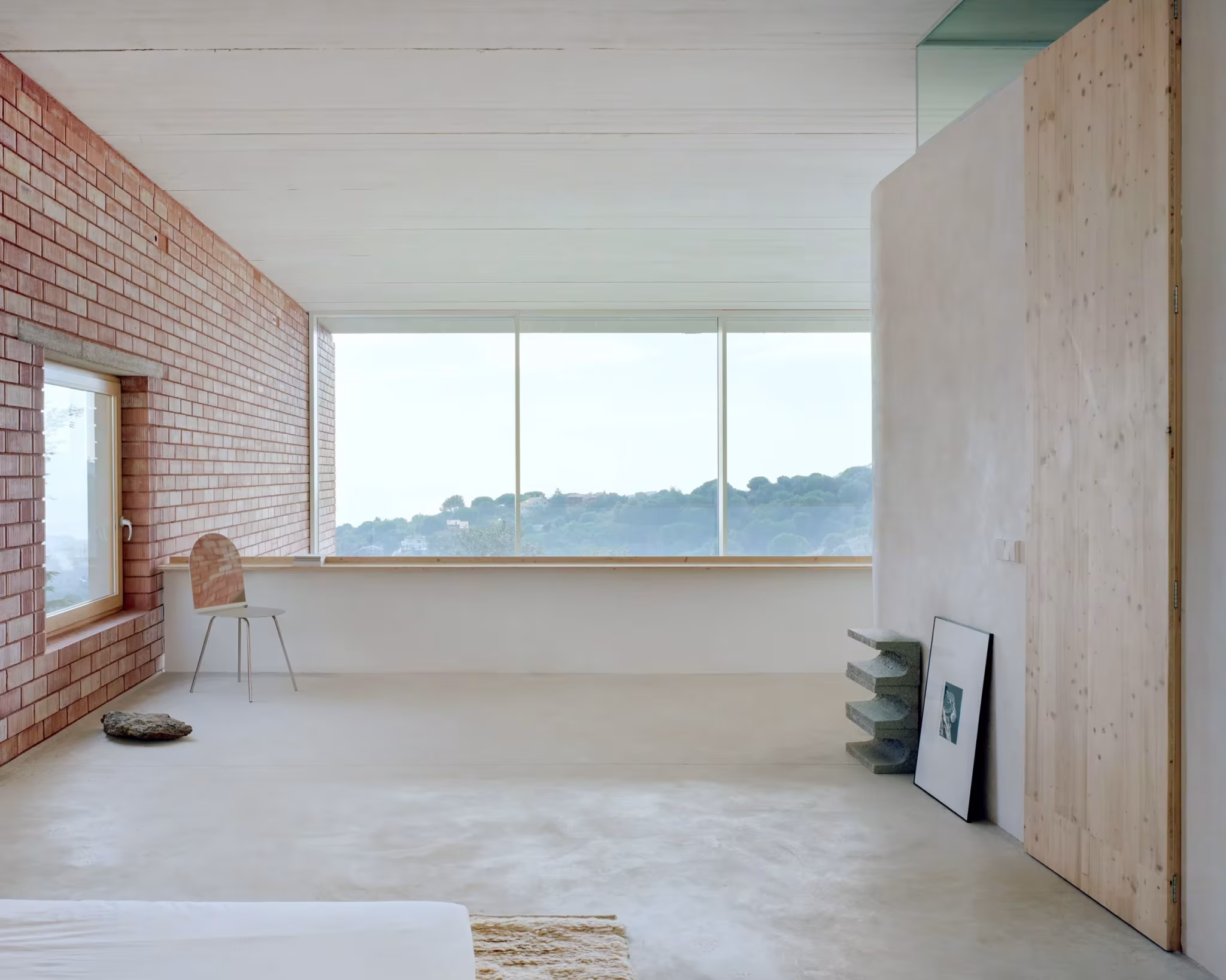 Dormitorio de la Casa Dosmurs con muro de ladrillo, panel de madera y ventana horizontal al paisaje